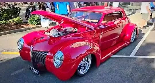 A custom red hot rod coupe with the bonnet up showing the engine