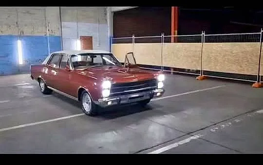 A classic Ford sedan with its headlights on inside the Carlo's Classic Muscle Cars showroom at Gepps Cross